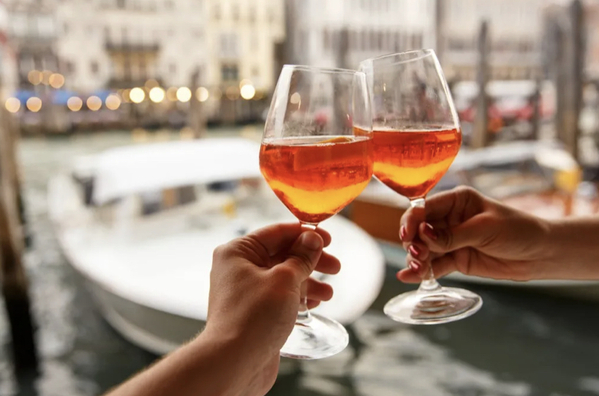 Two glasses with rosé wine clinking together being held by the stem with a male and female hand 